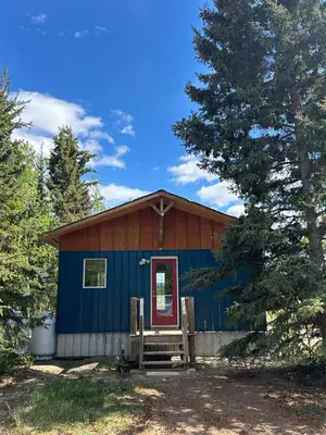 a blue cabin with a red door in the woods at Cabin with Fields of Dreams in Whitehorse