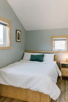 a bedroom with a large white bed with two windows at Roamer's Nook in Nordegg