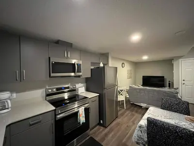 a kitchen with a stove top oven next to a living room at stylish 5-Star Suite 1BD 1 Bath Le Reve Beaumont in Nisku