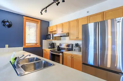 a kitchen with a stainless steel refrigerator and wooden cabinets at Boardwalk Bliss - Top Floor Downtown Condo in Canmore
