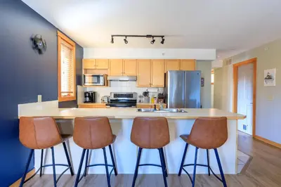 a kitchen with a counter with four bar stools at Boardwalk Bliss - Top Floor Downtown Condo in Canmore