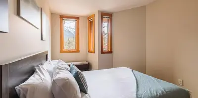 a bedroom with a bed and two windows at Mountainside - Stunning Views Downtown Location in Canmore