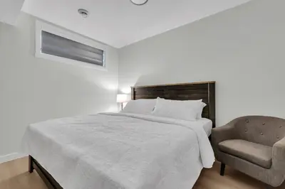 a white bedroom with a bed and a chair at Cozy Luxe Suite in Calgary
