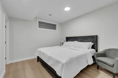 a white bedroom with a bed and a chair at Cozy Luxe Suite in Calgary