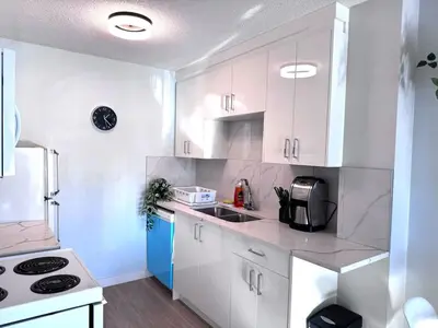 a white kitchen with white cabinets and a refrigerator at Stay Heart of Calgary, Enjoy Night Life, Free Parking Incl in Calgary