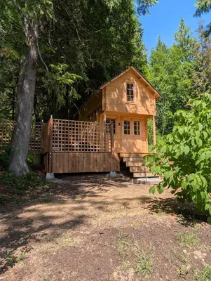 a small wooden house with a porch and a tree at Creekside Bunkies in Roberts Creek