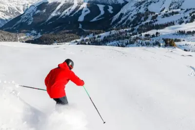 a person in a red jacket skiing down a snow covered slope at Chic Mountain View - Pool & HotTub - Fireplace - BBQ! in Canmore