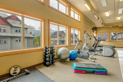 a gym with fitness equipment and windows in a house at Evergreen Escape - 2 Bedroom Condo with Pool & Hot Tub in Canmore
