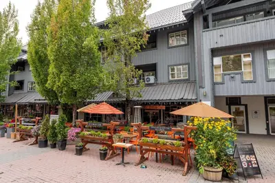 an outdoor cafe with tables and umbrellas in front of a building at Glacier Lodge 216 by Outpost Whistler in Whistler