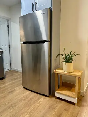 a stainless steel refrigerator in a kitchen with a table at Private Entire Guest Suite, 1 min to bus stops to Downtown and major attractions in Vancouver