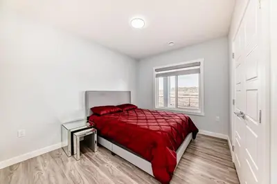 a bedroom with a bed with a red comforter and a window at 2 Beds, 1 bath Walkout Basement in Calgary
