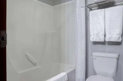 a white bathroom with a toilet and a tub and towels at Days Inn by Wyndham Whitecourt in Whitecourt