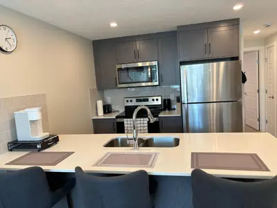 a kitchen with a sink and a stainless steel refrigerator at Cozy & Stylish AC Suite Near YYC Airport in Calgary