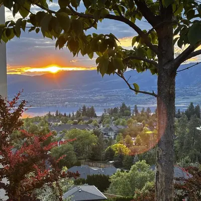 a sunset over a city from a tree at Hilltop Vistas Kelowna in Kelowna
