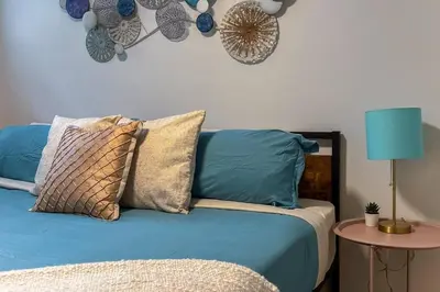 a blue bed with pillows and a table with a lamp at •SteamyRomanticBsmntSuite•KingBed•Wifi•Netflix in Edmonton