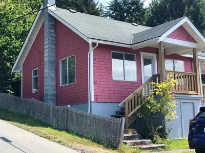 a red house with a porch and a fence at Sweet Home Alert Bay in Alert Bay