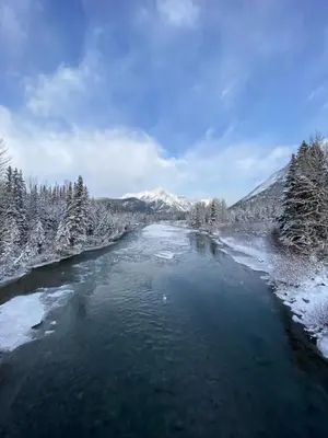 a river with snow covered trees and mountains in the background at Cozy Canmore resort with mt view hot tub and pool in Canmore