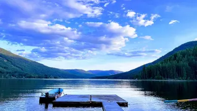 a dock on a lake with a boat in the water at Beachfront Lake House Moyie BC in Moyie