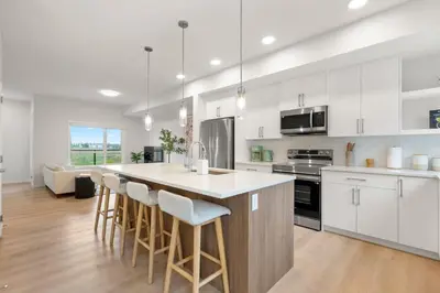 a kitchen with white cabinets and a island with bar stools at 3 Bedroom Luxurious Seton Town Home with Central AC and Lake View in Calgary