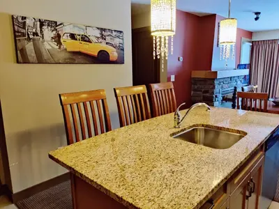 a kitchen with a sink and a counter with chairs at Best 2BR Canmore Stay, Banff, Wifi & Free Parking Incl in Dead Man's Flats