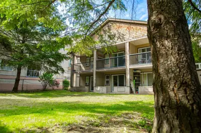 a large building with a tree in front of it at The Flats at Cedar Springs with Full Kitchen and Steps to Lake in Harrison Hot Springs