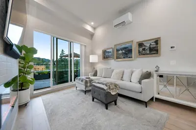 a living room with a white couch and large windows at Whirlaway – Luxurious one bedroom Penthouse with study and 2 parking spots by Victoria Prime! in Victoria