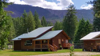 a log cabin in the woods with mountains in the background at Beatrice Place in Slocan