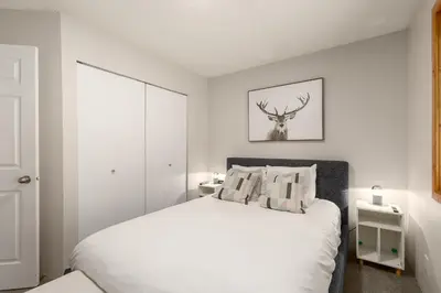 a white bedroom with a bed and a deer picture on the wall at 1BR in Powderview, Creekside, Bright and Cozy, Private Ski Storage, Fireplace, Free Parking in Whistler