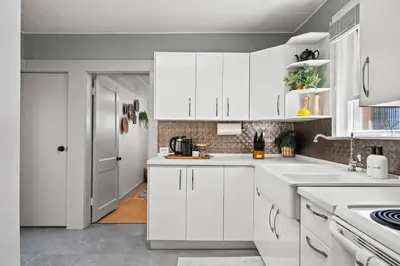 a white kitchen with white cabinets and a sink at The Canary 2BR Gem in Downtown Drumheller in Drumheller