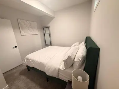 a bedroom with a bed with white sheets and a trash can at The Seton Nook - 1BR Suite Near Seton Health Campus, Cineplex and YMCA in Calgary