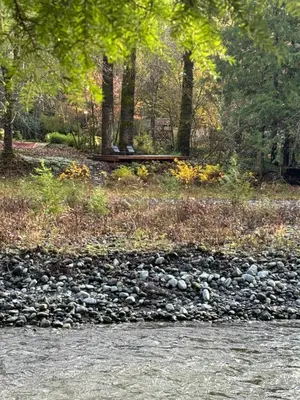 a river with rocks and trees and a bench at Riverwood Retreat-hot tub and cedar sauna on the river in Squamish