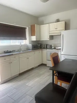 a kitchen with white cabinets and a table and a refrigerator at three bedroom near uvic in Victoria