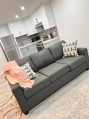 a gray couch in a living room with a kitchen at Cozy Corner - 1 bedroom suite - 15 mins from airport in Calgary