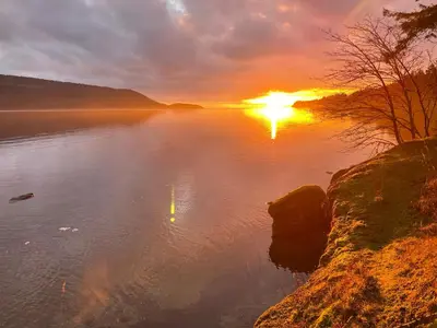 a sunset on a lake with the sun setting at Cokely Cove Guesthouse - Oceanside Villa in Denman Island