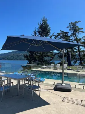 a blue umbrella over a table and chairs next to a pool at Cokely Cove Guesthouse - Oceanside Villa in Denman Island