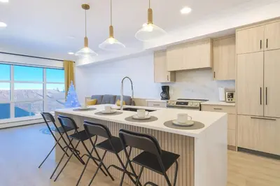 a kitchen with a large white island with chairs at Family Modern 1BR and Den Condo - Apartment with City View, Downtown, Balcony, Free Parking & In-Suite Laundry! in Calgary