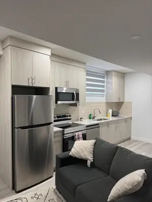 a kitchen with a couch and a stainless steel refrigerator at Cozy Inn new basemt wt sep entrance contains 1 bdrm and den for up to 4 guests in Airdrie