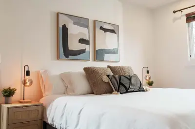 a bedroom with a white bed with three pictures on the wall at 4 Bed Home Along River Near DT AC Hot Tub in Calgary