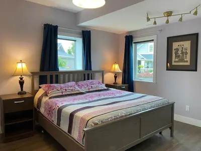 a bedroom with a bed and two windows with blue curtains at Relaxing Lakeview 2 bedroom entire suite in Kelowna