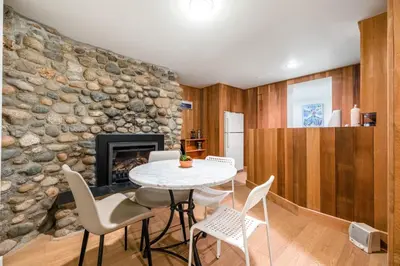 a living room with a table and chairs and a stone wall at Picturesque room surrounded by flowers with share spaces in Vancouver