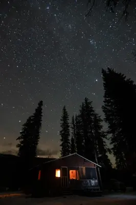 a cabin under a night sky with stars and trees at Off-Grid Mountain Lodge & 4 Cabins - Sauna, Hot Tub & Fishing in Rock Lake Provincial Park