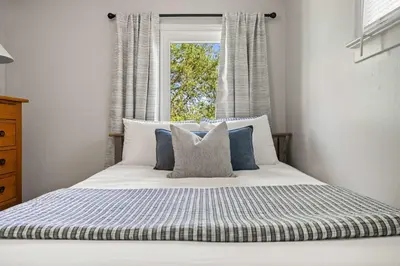 a bed with blue and white pillows and a window at Kinepik Cottage Sunroom with Beach Access in Sylvan Lake