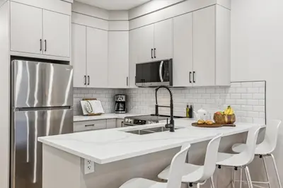 a kitchen with white cabinets and a stainless steel refrigerator at Ultimate Group Stay, 3 King Beds, 2 Suites in Calgary