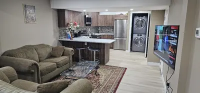 a living room with two couches and a kitchen at Cozy and Affordable Apartment - Guesthouse South West Airdrie in Airdrie