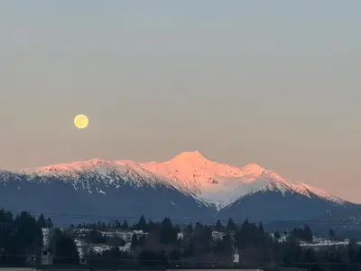 a moonrise over a mountain range with a town and a city at Beautiful home near City centre! in Kitimat