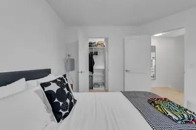 a white bedroom with a bed with a black and white pillow at 1P Culture - Sara in Calgary