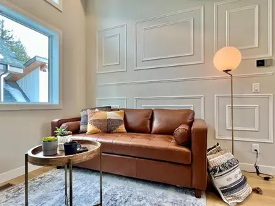 a living room with a brown couch and a table at Stunning View New Townhome Sleeps 11 AC and Hot Tub in Canmore