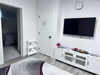 a white living room with a flat screen tv on a wall at 2 Bedroom snug retreat in Livingston Calgary Alberta in Calgary