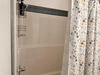 a shower with a white shower curtain with a shower at 2 Bedroom snug retreat in Livingston Calgary Alberta in Calgary