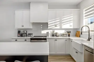 a white kitchen with white cabinets and a sink at King Bed, AC, Fenced Yard, Family Friendly, 5 min South Health Campus in Calgary